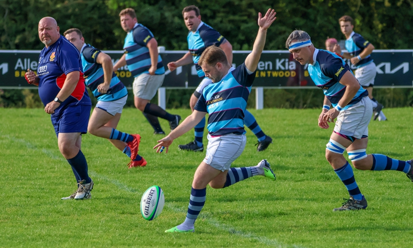 rugby players on rugby pitch with 1 player kicking rugby ball